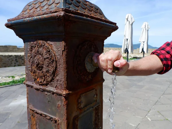 Alghero, İtalya 'daki gezinti alanının dışında paslı bir çeşme var. Erkek musluğu tutuyor ve içmek için düğmeye basıyor..