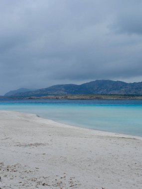 İtalya 'nın Sardinya adasındaki ünlü Stintino plajının üzerinde karamsar değişen hava. Gri ağır bulutlar. Aquamarine mavi suyu. Dikey fotoğraf.