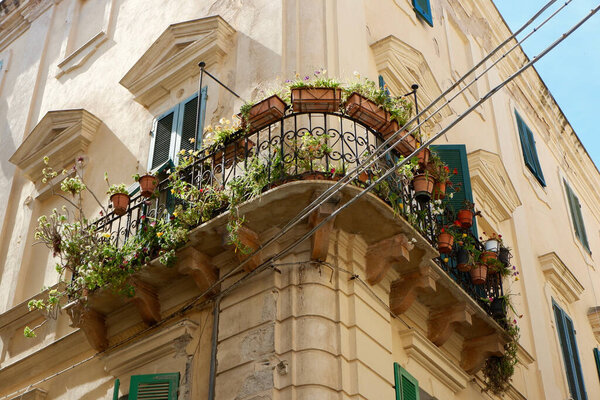 Vintage old-fashioned balcony decorated with home plants seen from street outside in Alghero, Sardinia, Italy. Italian real life scene.