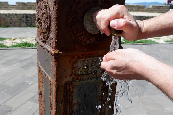 Close-up of old weathered fountain with dripping water. Male washing hands on the antique street.