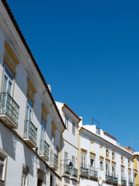 Line of old fashioned vintage facades of white colour against clear sky in Evora Portugal vertical backdrop. clipart