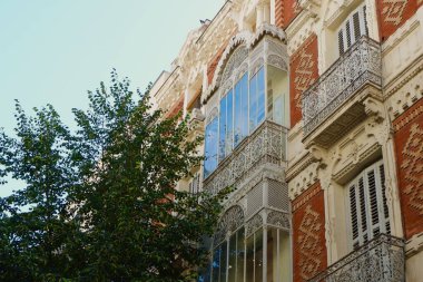 Eski balkonlar kıvrımlı demir korkuluklar İspanya 'nın başkenti Madrid' in canlı yeşilliklerinden görünen eski moda ön cephe üzerine beyaz renklerle boyanmış..