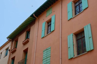 Resimli bir binada mercan renkli duvarlar ve büyüleyici turkuaz panjurlar bulunur. Berrak mavi gökyüzü, sakin mahallenin sakin atmosferine ekleniyor..