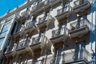 Tarihi bina, süslü korkulukları olan karmaşık balkonlara ev sahipliği yapıyor. Mimari klasik Avrupa tarzını sergiliyor. Arkaplan olarak parlak mavi gökyüzü, canlı bir atmosfer yaratıyor..