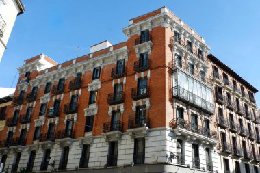 Çok güzel detaylandırılmış, süslü balkonları olan kırmızı tuğlalı bir bina kalabalık bir kentsel alanda duruyor. Açık mavi gökyüzü bu tarihi yapının mimari özelliklerini artırır. Madrid, İspanya