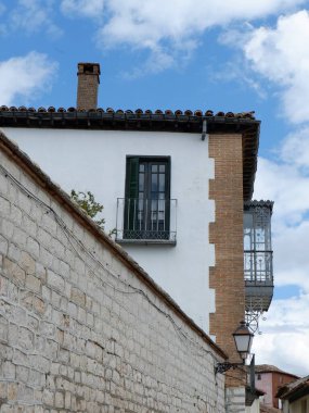 Büyüleyici beyaz bir taş bina, yeşil bir balkona sahip, mavi gökyüzü ve beyaz bulutlardan oluşan tipik bir köye karşı tarihi bir mimari sergiliyor..