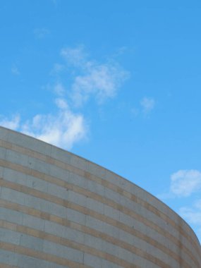 Kavisli taş yapısı, doğal ışıkla yıkanırken çağdaş mimari tarzı yansıtır. Parlak mavi gökyüzü konumun görsel çekiciliğini ve geniş ambiyansını arttırır.