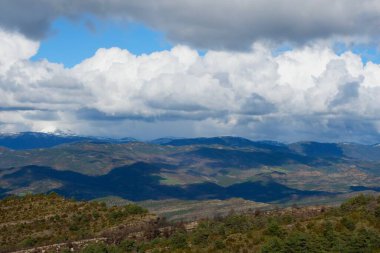 Bereketli yeşil tepeler dağlarda açık bir günde dramatik bulutlarla dolu uçsuz bucaksız bir gökyüzünün altında uzanıyor. Güneş ışığı manzaranın dış hatlarını ve dokularını çok güzel aydınlatıyor..