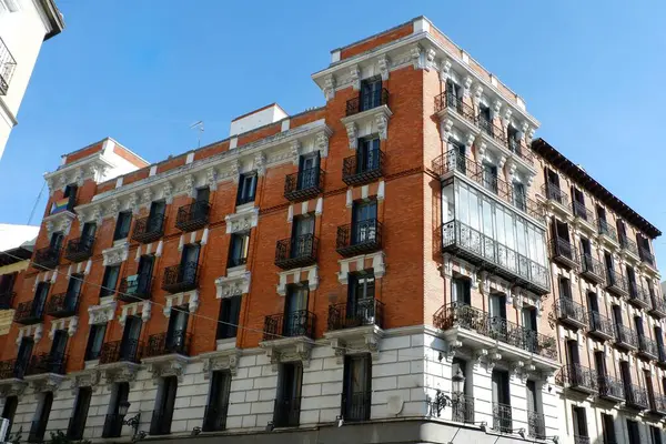 Çok güzel detaylandırılmış, süslü balkonları olan kırmızı tuğlalı bir bina kalabalık bir kentsel alanda duruyor. Açık mavi gökyüzü bu tarihi yapının mimari özelliklerini artırır. Madrid, İspanya