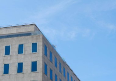 Geniş pencereli çağdaş bir bina parlak mavi bir gökyüzüne karşı duruyor. Yapıda düz bir çatı ve modern mimari sergilenen cam paneller yer alıyor..