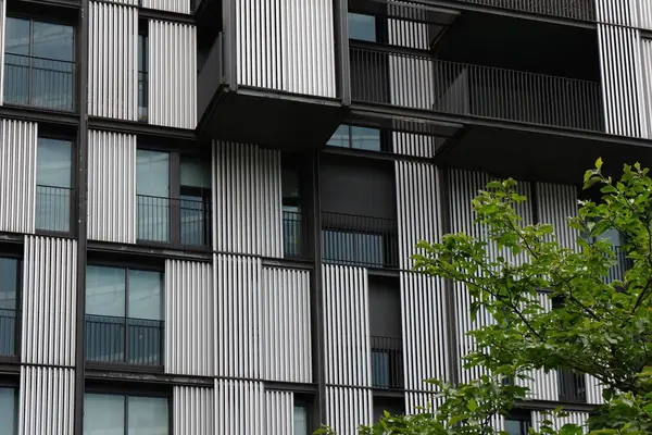 Çağdaş bir binada dikey çizgileri ve geniş pencereleri olan çarpıcı bir cephe vardır. Bereketli yeşil ağaçlar modern kentsel çevreye karşıtlık ekler.