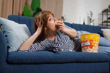 Genç kadın film izlemeye, kanepede yatarken patlamış mısır yemeye odaklanmış.