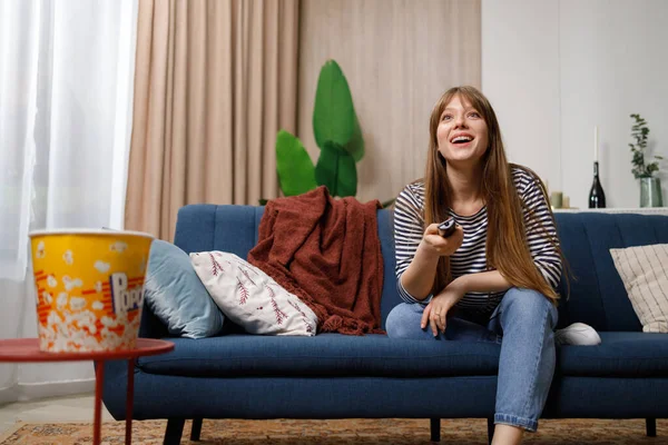 Kanepede Otururken Uzaktan Kumandayla Televizyon Izleyen Mutlu Bir Genç Kadın — Stok fotoğraf