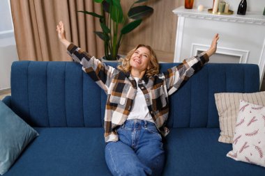 Neşeli gülüşlü olgun bir kadın rahat bir koltukta dinleniyor ve geriye yaslanarak vücudunu esnetiyor.