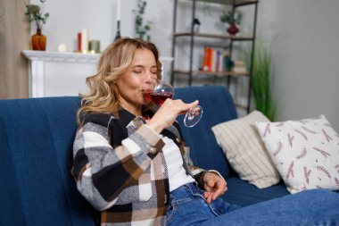 Orta yaşlı, güzel bir kadının portresi. Kanepede yalnız başına şarap içiyor.