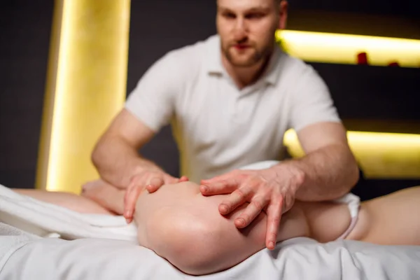 Male physiotherapist massages the legs of a woman in a spa center