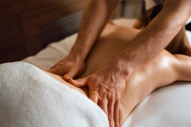 Close-up of masseur's hands doing back massage to young woman