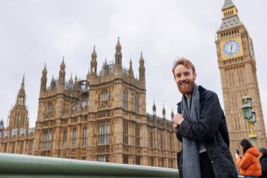 Londra 'da Big Ben' in önünde sırt çantalı mutlu 30 'lu yaşlarda bir adam.