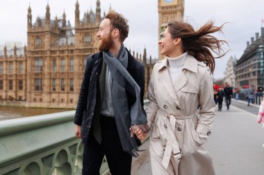 Mutlu genç çift, Londra 'nın Big Ben' inin arka planında el ele tutuşarak yürüyor.