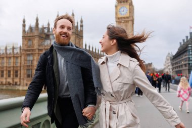 Mutlu genç çift, Londra 'nın Big Ben' inin arka planında el ele tutuşarak yürüyor.