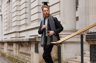 Ceketli ve atkılı şık sakallı adam binadan çıkarken merdivenlerden iniyor.