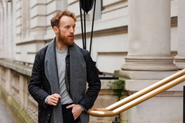 Yakışıklı, sakallı adam binadan dışarı çıkıyor.