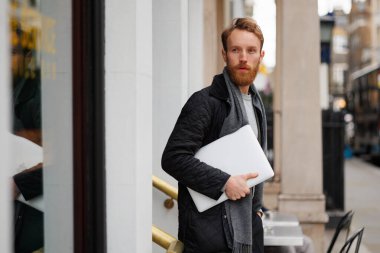 Elinde dizüstü bilgisayarı olan ciddi bir iş adamı binadan ayrılıyor ve başka yere bakıyor.