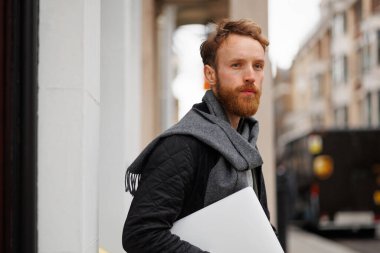 Elinde dizüstü bilgisayarı olan ciddi bir iş adamı binayı terk ediyor.