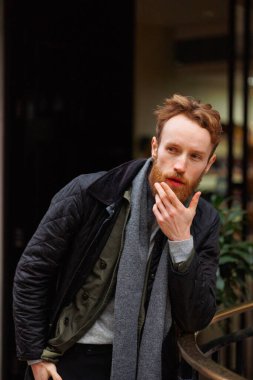 Dışarıda poz veren düşünceli adam korkuluklara yaslanıyor.