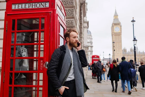 Człowiek Rozmawia Przez Smartfona Stojąc Londyńskiej Ulicy Pobliżu Czerwonej Budki — Zdjęcie stockowe