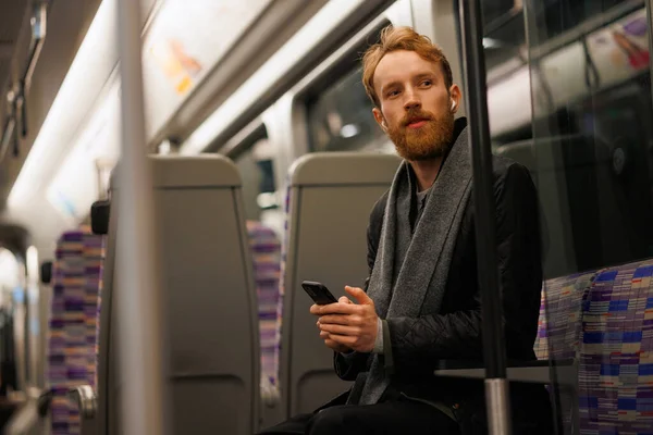 턱수염을 남자가 지하철에 스마트폰으로 헤드폰을 음악을 — 스톡 사진
