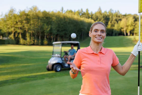 Elated Golfer: Woman Celebrates by Finish Flag, Man Drives Cart