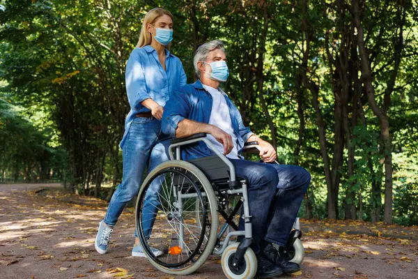 Empowering Compassion: Woman with Mask Helping Man in Wheelchair Outdoors