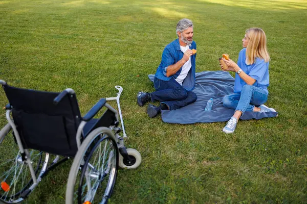 Outdoor Dining Delight: Nurse and Handicapped Man Share Picnic Feast