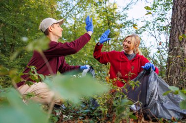 Çevre bakımıyla motive olan genç adam ve kadın, ormanı çöplerden temizlerken birbirlerine beşlik çakıyorlar. Doğayı temizleyen yeşil aktivistler