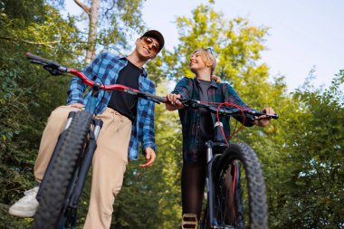 Düşük açılı erkek ve kadın bisikletle doğada duruyor.