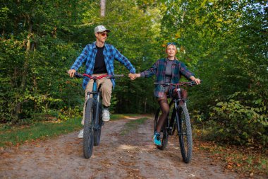 Ormanda bisiklete binen mutlu çift el ele tutuşuyor.