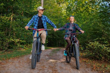 Ormanda bisiklete binen mutlu çift el ele tutuşuyor.