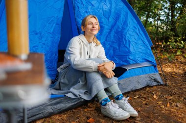 Şirin genç bir bayan doğada bir çadırda oturuyor.