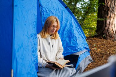 Doğada bir çadırda oturmuş kitap okuyan sevimli bir kadın.