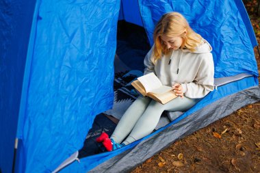 Doğayla baş başa çadırda oturmuş kitap okuyan bir kadın.