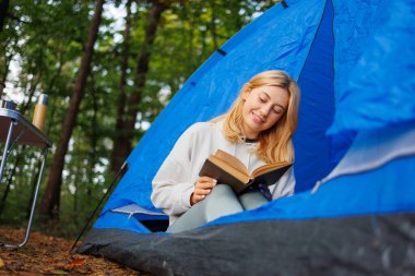 Kamp çadırında kitap okuyan neşeli kız.
