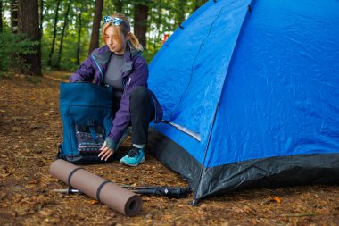 Orman kampında çadırın yanında sırt çantasıyla gezen genç bir turist.