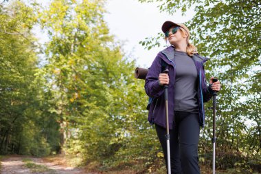 Güneşli orman yolunda yürüyüş direğiyle yürüyen maceraperest kadın.