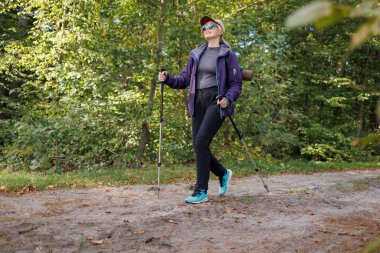 Ormanda yürüyüş yapan aktif bir kadın. Direkleri olan, açık hava maceralarından hoşlanan.