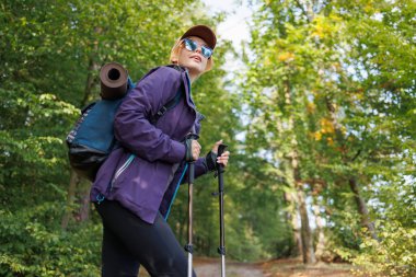 Sırt çantalı ve ormanda yürüyüş yapan sırıklı kadın turist.