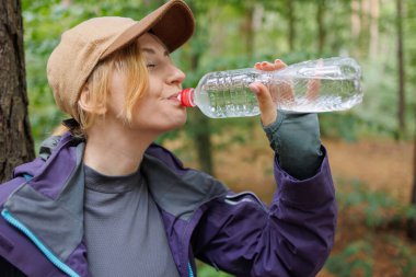 Orman yürüyüşü sırasında plastik şişeden su içen kadın yürüyüşçülere yakın çekim