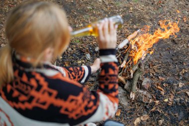 Ateşle bira içen ve orman kampında yemek kızartan kampçı kadın.