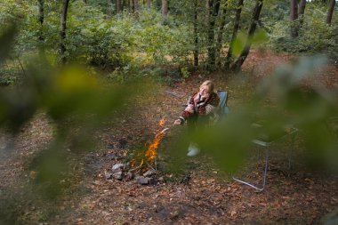 Ormanda kamp ateşinin yanında oturan kampçı kadın.