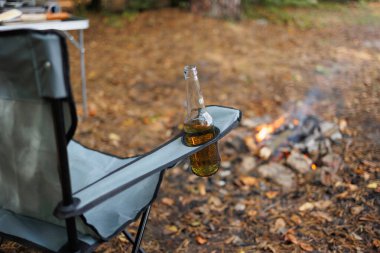 Bira şişesi, kamp ateşinin yanındaki koltuğun cebinde.